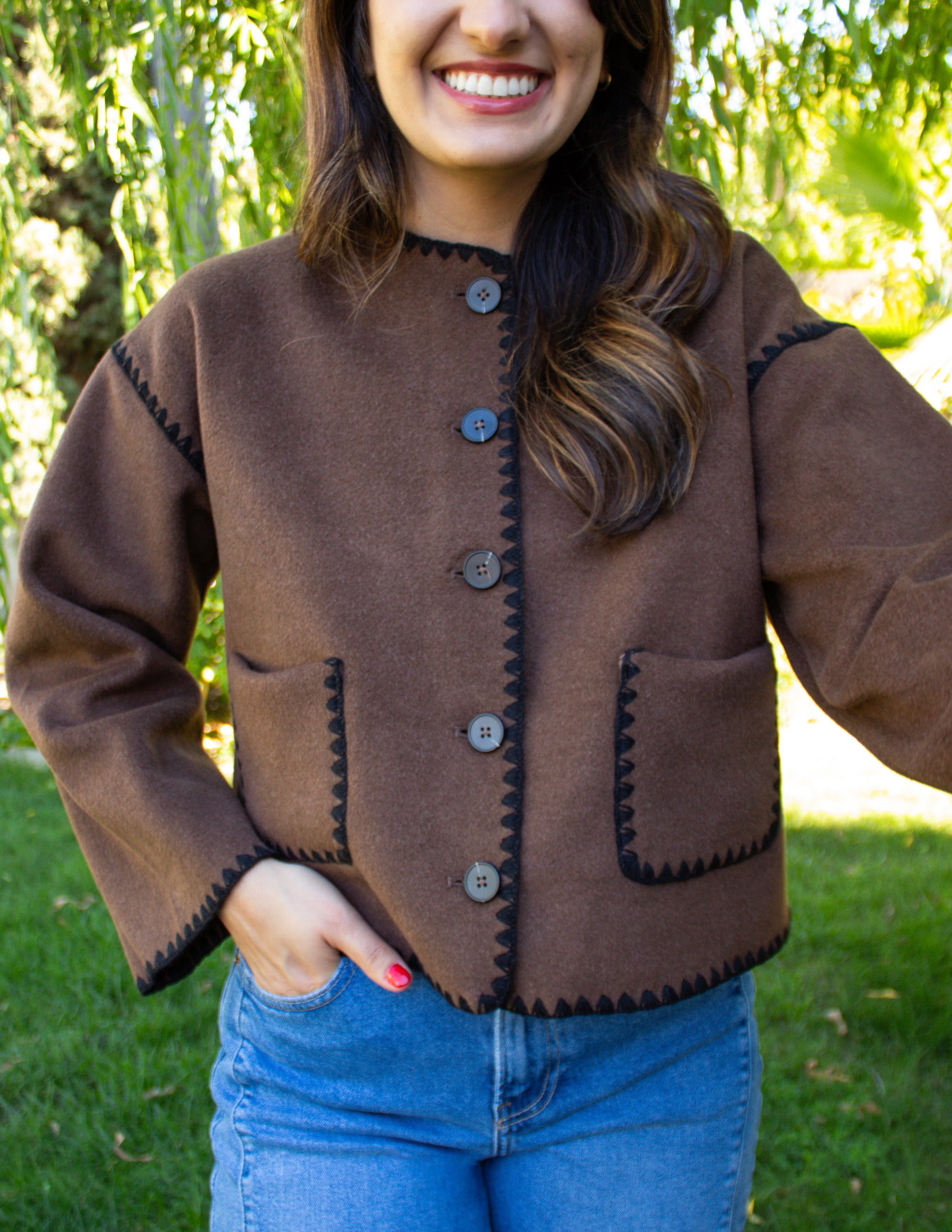 Woman wearing a brown jacket with black stitching outdoors