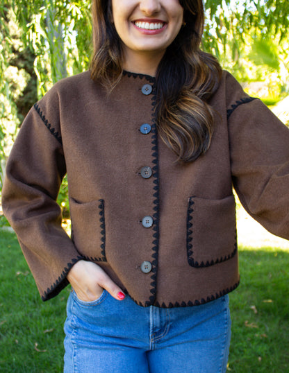 Woman wearing a brown jacket with black stitching outdoors