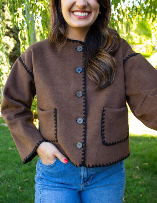 Woman wearing a brown jacket with black stitching outdoors